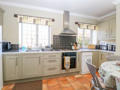 A kitchen with cabinets a stove a dishwasher two windows and a table with chairs at The Meadows Cottage in Billingford near Bawdeswell
