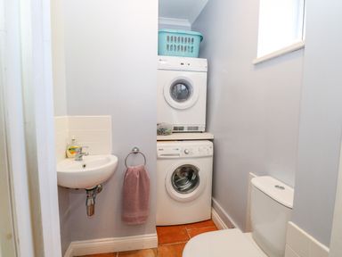 A small laundry room with a stacked washer and dryer a sink with soap a towel hanging and a toilet at The Meadows Cottage in Billingford near Bawdeswell