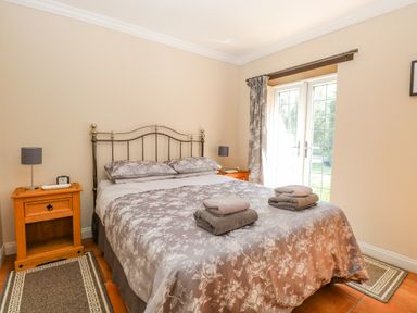 A bedroom with a double bed two bedside tables lamps patterned curtains and folded towels on the bed at The Meadows Cottage in Billingford near Bawdeswell