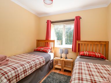A bedroom with two single beds with plaid bedding and red curtains at The Meadows Cottage in Billingford near Bawdeswell