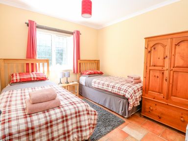 A bedroom with two single beds a wooden wardrobe and a window with red curtains at The Meadows Cottage in Billingford near Bawdeswell