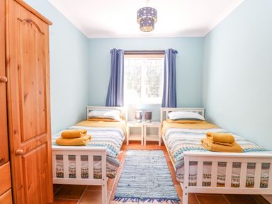 A bedroom with two single beds a wooden wardrobe a window with curtains and a rug on the floor at The Meadows Cottage in Billingford near Bawdeswell