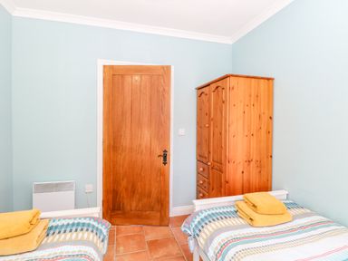 A bedroom with two single beds, a wooden door, and a wooden wardrobe at The Meadows Cottage in Billingford near Bawdeswell