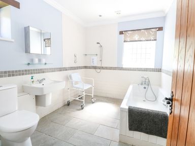 A bathroom with a toilet sink bath and a shower chair at The Meadows Cottage in Billingford near Bawdeswell