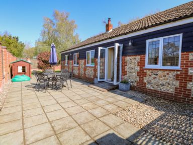 A patio with metal table and chairs and an umbrella outside a brick and stone house at The Meadows Cottage in Billingford near Bawdeswell
