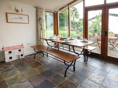 A dining area with a wooden table and benches set with dishes next to large windows overlooking a garden at Gatehouse in Painscastle