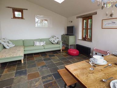 A living room with a green sofa a wooden dining table and a television on a green cabinet at Gatehouse in Painscastle