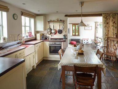 A kitchen with cream cabinets wooden countertops a dining table with chairs and pots hanging above a stove at Gatehouse in Painscastle