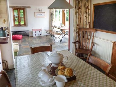 A dining area with a table set for tea and a seating area with benches and a dollhouse at Gatehouse in Painscastle