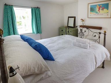 A bedroom with a metal bed frame and white bedding with blue pillows a green dresser with a mirror and flowers curtains on the window and a wall picture at Gatehouse in Painscastle