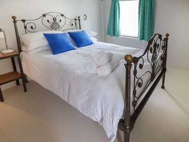 A bedroom with a metal bed frame with white bedding blue pillows and rolled towels at Gatehouse in Painscastle