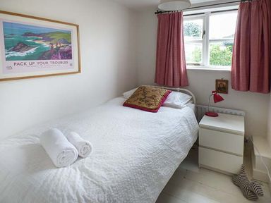 A bedroom with a white bedspread two rolled white towels a bedside table with a red lamp and pink curtains at Gatehouse in Painscastle