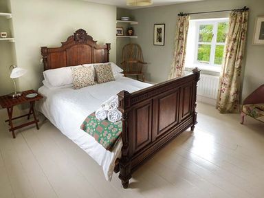 A bedroom with a wooden bed frame white bedding and floral curtains at Gatehouse in Painscastle