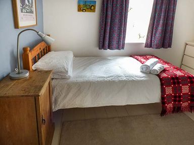 A bedroom with a single bed with white bedding and a red blanket and two rolled white towels on the bed at Gatehouse in Painscastle