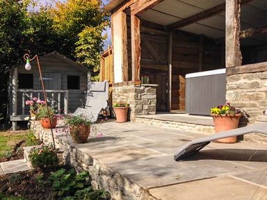 A stone patio with lounge chairs and potted plants next to a wooden structure and a small grey shed in a garden at Gatehouse in Painscastle
