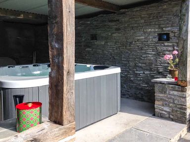 A hot tub in a stone and wood outdoor covered area with a small plant on a stone ledge at Gatehouse in Painscastle