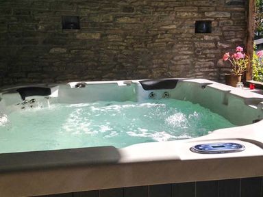 An outdoor hot tub with water jets against a stone wall with a flower pot on the side at Gatehouse in Painscastle