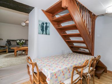 A dining area with a wooden table covered by a floral tablecloth and wooden chairs near a wooden staircase at The Coach House in Bitton
