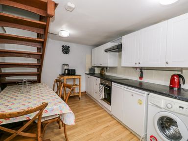 A kitchen with wooden stairs a dining table with chairs white cabinets and various appliances at The Coach House in Bitton