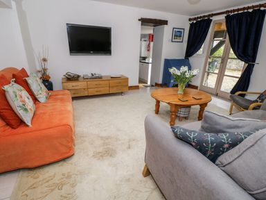A living room with an orange sofa a gray sofa a wooden coffee table and a wall-mounted television at The Coach House in Bitton