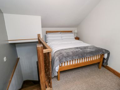 A bedroom with a wooden bed and gray blanket next to a wooden staircase at The Coach House in Bitton