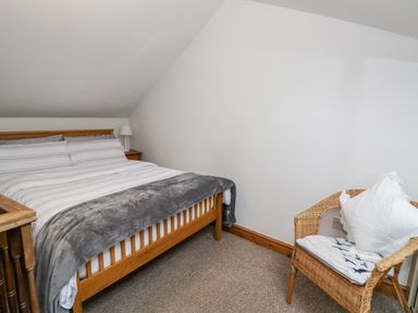 A bedroom with a wooden bed a bedside table with a lamp and a wicker chair with a cushion at The Coach House in Bitton