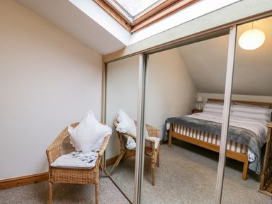 A bedroom with a bed bedside tables and a chair in front of mirrored sliding closet doors at The Coach House in Bitton