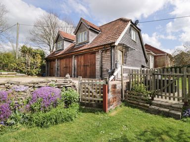 A wooden house with three garage doors surrounded by a garden with purple flowers and green grass at Shephard's Retreat in Charlton Mackrell near Somerton