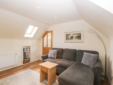 A living room with a gray sectional sofa wooden side table framed wall art bookshelf and an arched floor lamp at Shephard's Retreat in Charlton Mackrell near Somerton