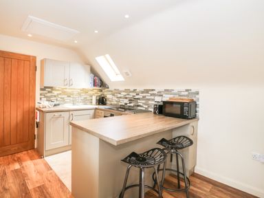 A small kitchen with a wooden countertop, two black stools, a microwave, a kettle, and white cabinets at Shephard's Retreat in Charlton Mackrell near Somerton
