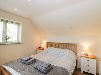 A bedroom with a wooden bed with checkered bedding two bedside tables with lamps and a window with blinds at Shephard's Retreat in Charlton Mackrell near Somerton