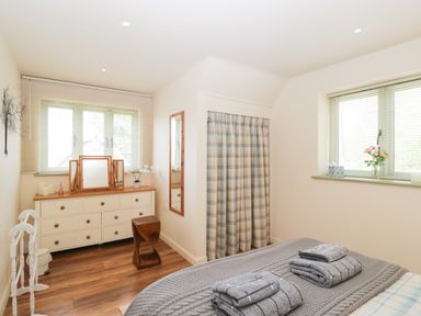 A bedroom with a bed, dresser, mirror, wooden floor and windows with blinds at Shephard's Retreat in Charlton Mackrell near Somerton
