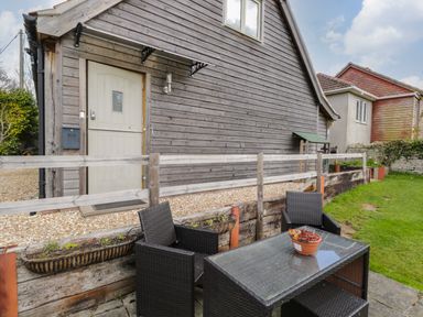 An outdoor seating area with two black wicker chairs and a glass table with a potted plant by a wooden building at Shephard's Retreat in Charlton Mackrell near Somerton