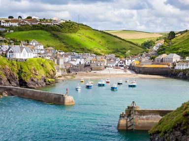 A coastal village with boats in the harbor and green hills in the background at High Tide in Rock