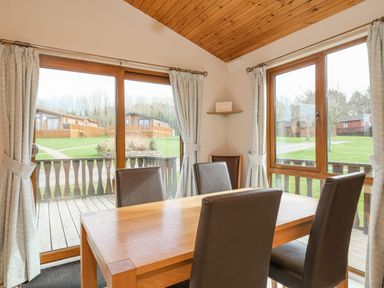 A dining area with a wooden table and four chairs next to large windows overlooking a green outdoor area at High Tide in Rock