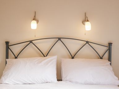 A bed with white pillows and a metal headboard with two wall-mounted lights above at High Tide in Rock