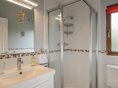 A bathroom with a sink and mirror a glass shower enclosure and a window with a red blind at High Tide in Rock