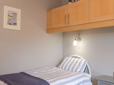 A bedroom with a single bed with striped bedding a wall lamp wooden overhead cabinets and a framed picture at High Tide in Rock