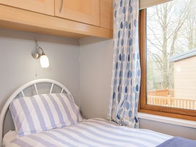 A bedroom with a single bed with striped bedding and a window with patterned curtains at High Tide in Rock
