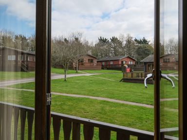 A view through a window showing green lawns, leafless trees, paths, and wooden cabins at High Tide in Rock