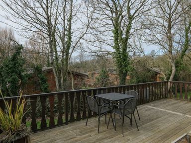 A wooden deck with a metal table and four chairs surrounded by trees and wooden cabins at High Tide in Rock
