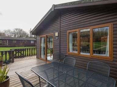 A wooden deck with a metal table and chairs outside a log cabin at High Tide in Rock