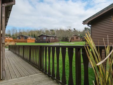 A view from a wooden deck overlooking grassy area and several wooden lodges at High Tide in Rock