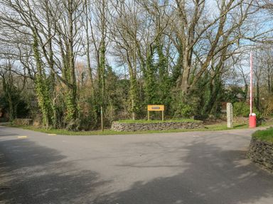 A road fork with a stone wall and trees in a wooded area with a sign that reads The Glade