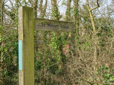 A wooden signpost for St Minver Village on a public footpath surrounded by trees and bushes at High Tide in Rock