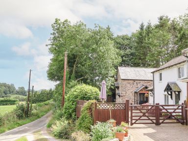 A countryside home with a stone building and wooden gate near a narrow road with trees at The Old Barn in Llanferres near Ruthin