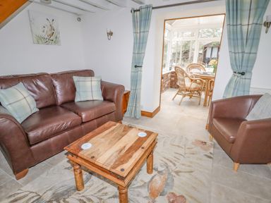 A sitting room with brown leather chairs a wooden coffee table and a view into a dining area with wicker furniture at The Old Barn in Llanferres near Ruthin
