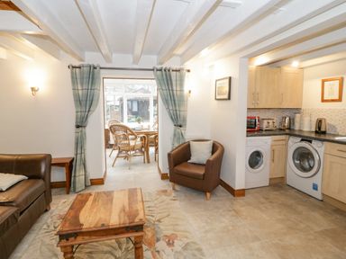 A living area with a brown leather sofa a wooden coffee table a brown armchair and kitchen appliances including a washing machine and dryer at The Old Barn in Llanferres near Ruthin