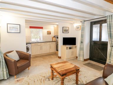 A kitchen and living area with a wooden coffee table brown armchairs a TV on a cabinet and a black door with curtains at The Old Barn in Llanferres near Ruthin