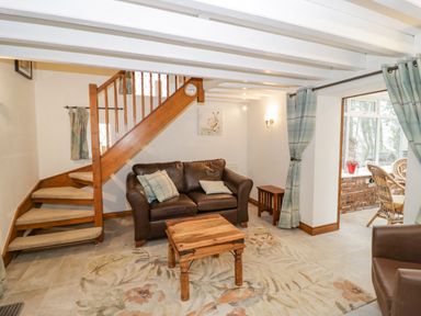 A living room with a brown leather sofa a wooden coffee table and a staircase at The Old Barn in Llanferres near Ruthin